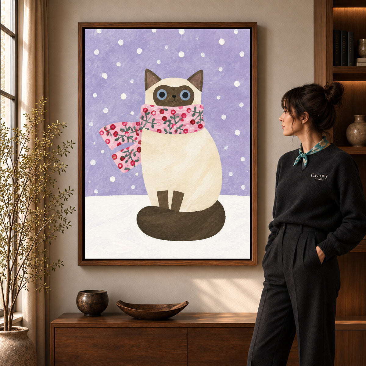Winter cat canvas art in a walnut frame beside a standing woman and wooden console.