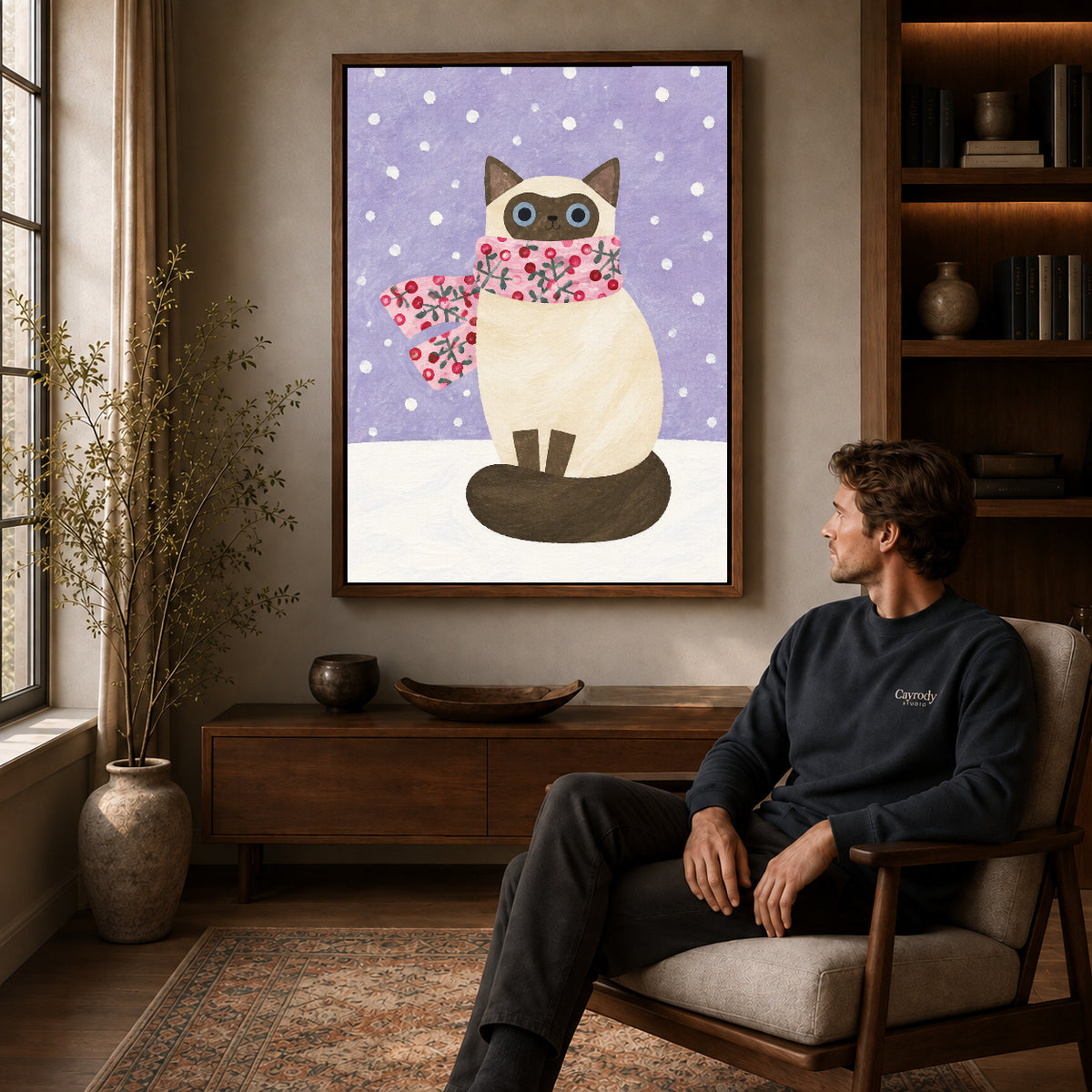 Winter cat canvas art in a walnut frame above a console beside a seated man.
