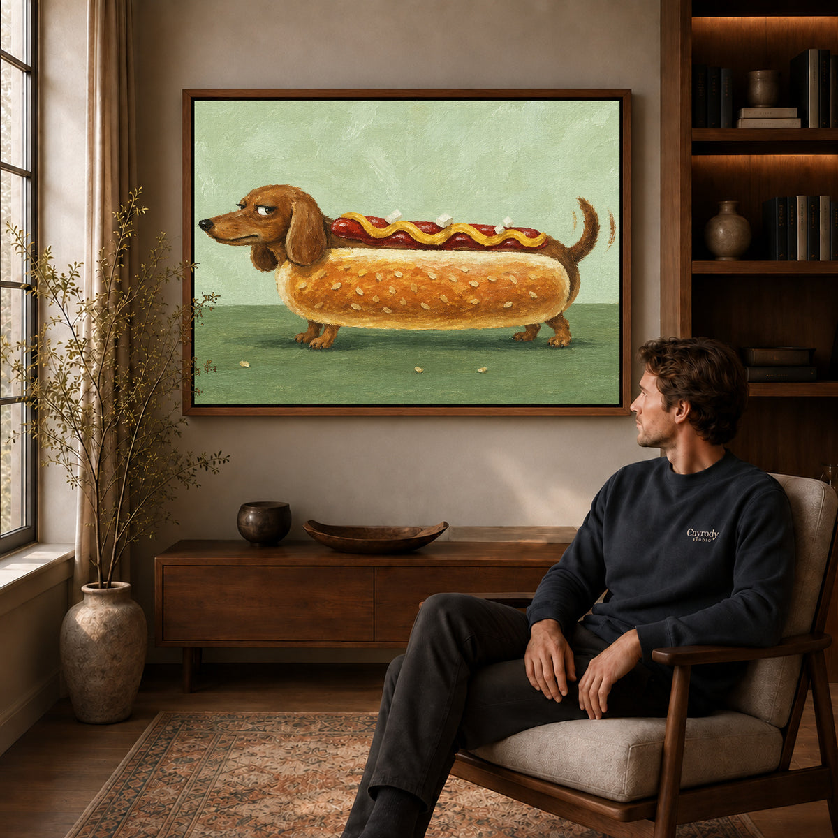 Dachshund hot dog canvas art in a walnut frame above a console beside a seated man.