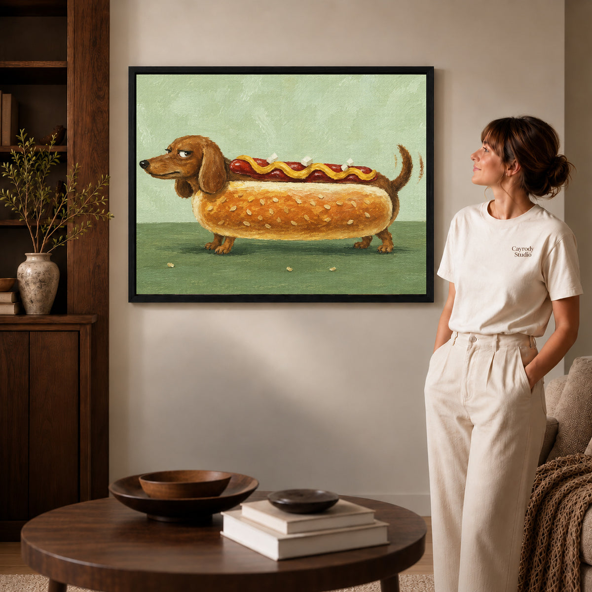 Dachshund hot dog canvas art in a black frame beside a woman and round wooden table.