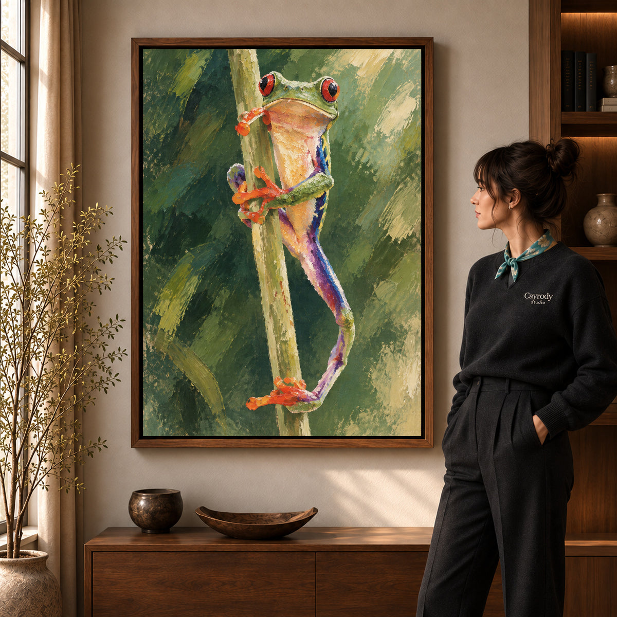 Tree frog canvas art in a walnut frame beside a standing woman and wooden console.