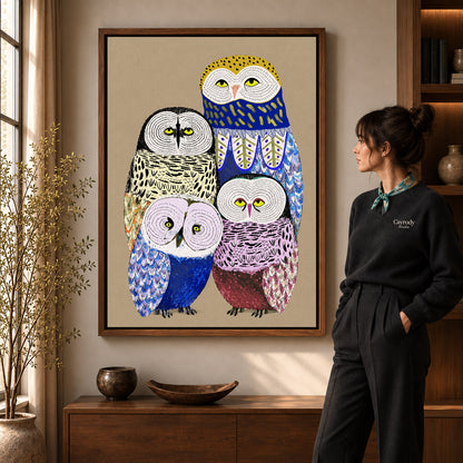 Owl family canvas art in a walnut frame beside a standing woman and wooden console.