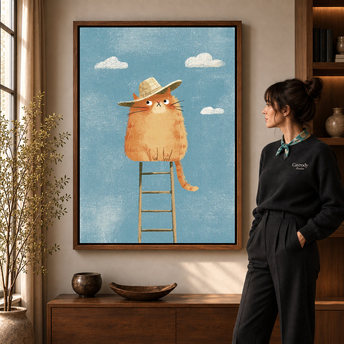 straw hat cat canvas art in a walnut frame beside a standing woman and wooden console.