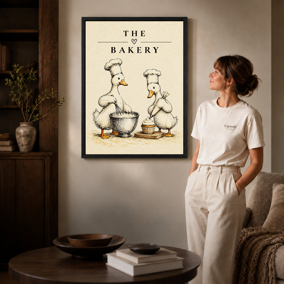 vintage bakery ducks canvas art in a black frame beside a woman and round wooden table.