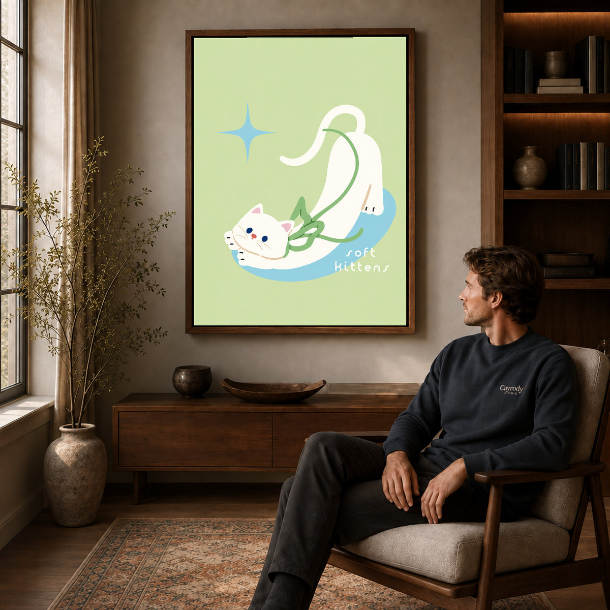 stretching white kitten canvas art in a walnut frame above a console beside a seated man.