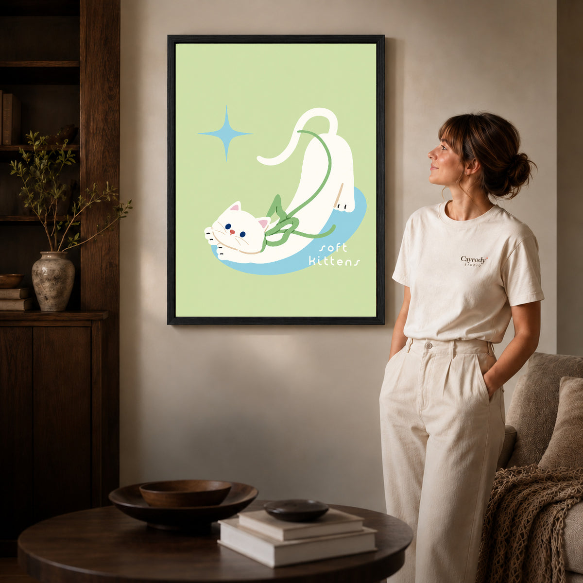 stretching white kitten canvas art in a black frame beside a woman and round wooden table.