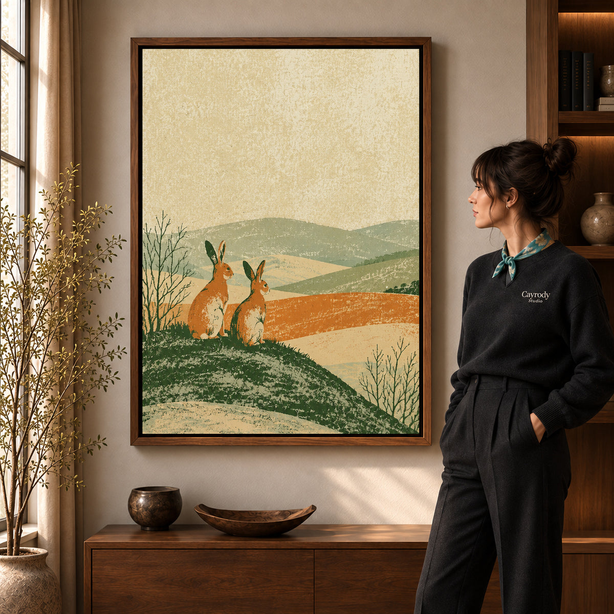 rustic rabbit landscape canvas art in a walnut frame beside a standing woman and wooden console.