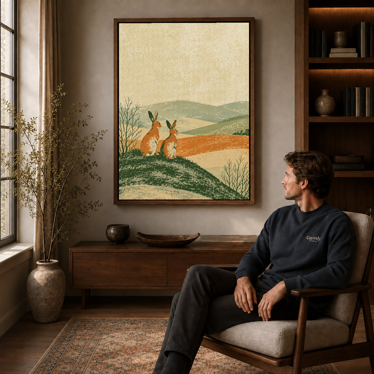 rustic rabbit landscape canvas art in a walnut frame above a console beside a seated man.