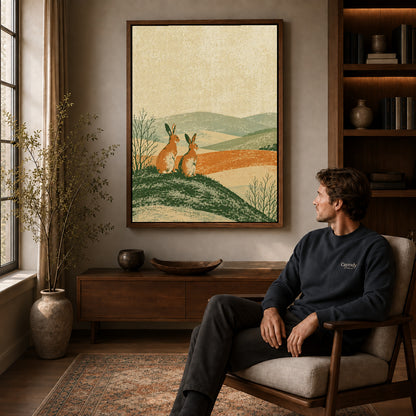 rustic rabbit landscape canvas art in a walnut frame above a console beside a seated man.