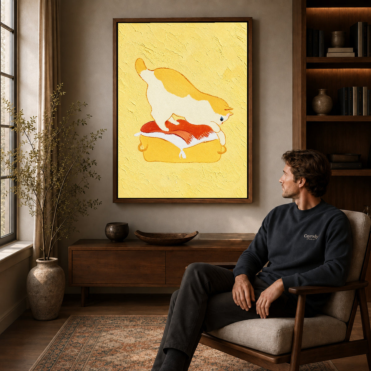 playful kneading cat canvas art in a walnut frame above a console beside a seated man.
