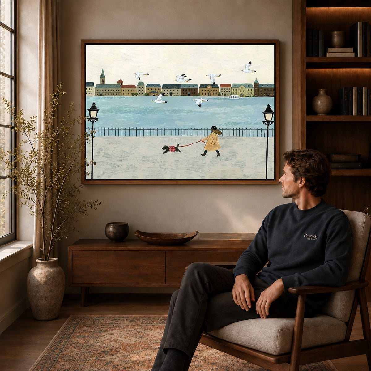 folk waterfront walk canvas art in a walnut frame above a console beside a seated man.