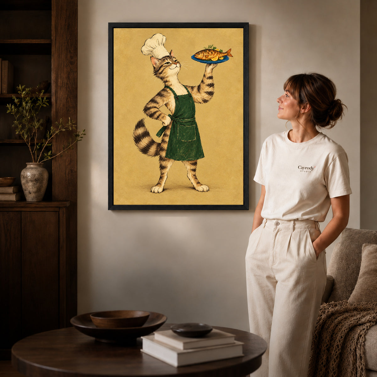 vintage fish chef cat canvas art in a black frame beside a woman and round wooden table.