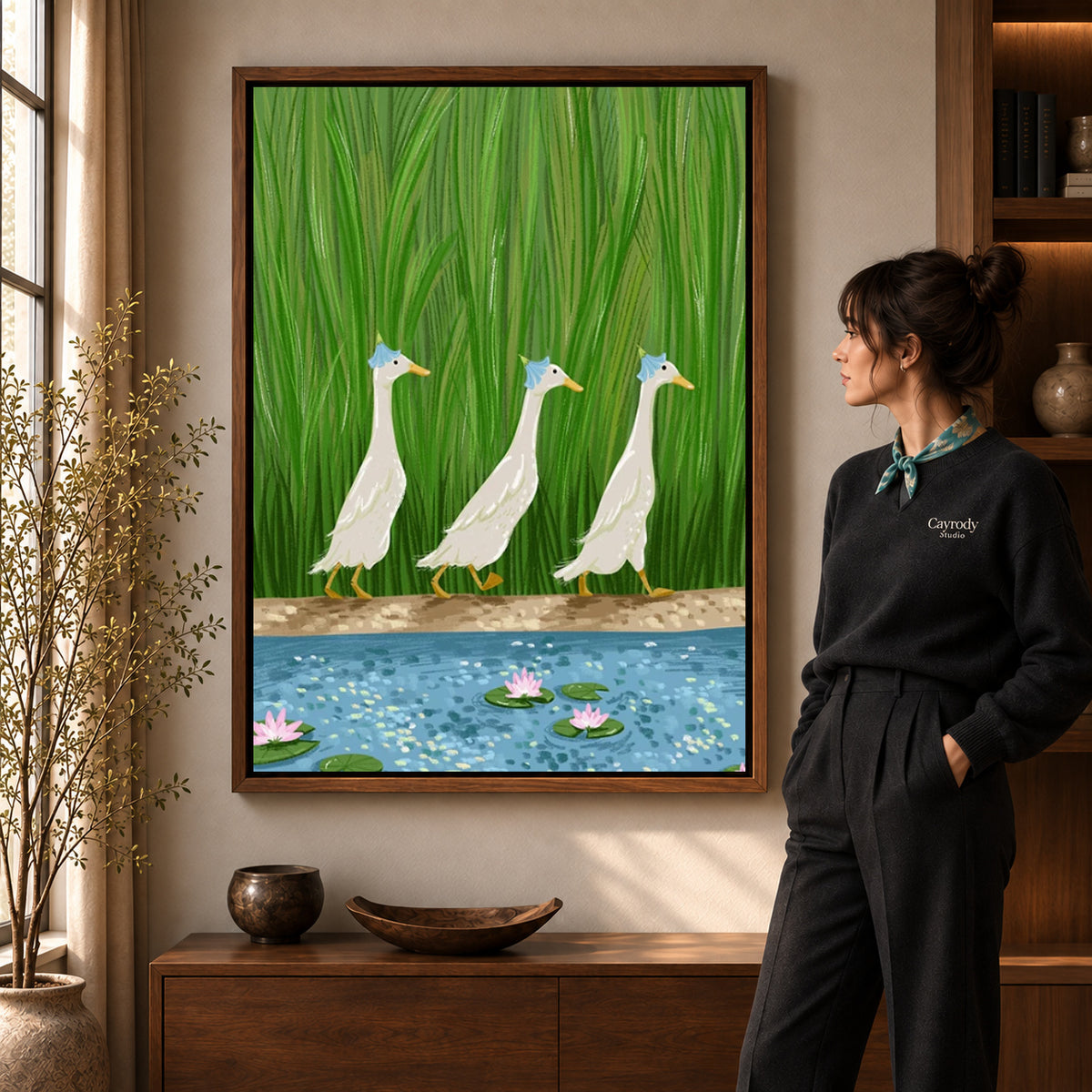 folk pond geese canvas art in a walnut frame beside a standing woman and wooden console.