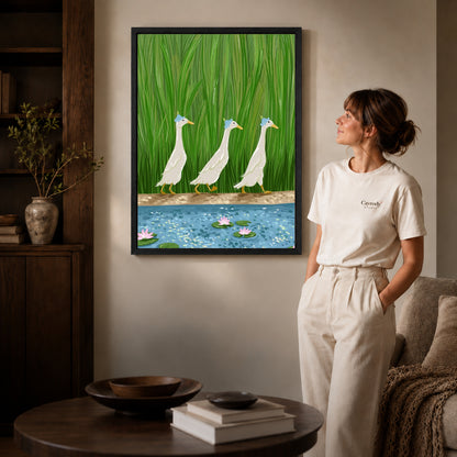 folk pond geese canvas art in a black frame beside a woman and round wooden table.