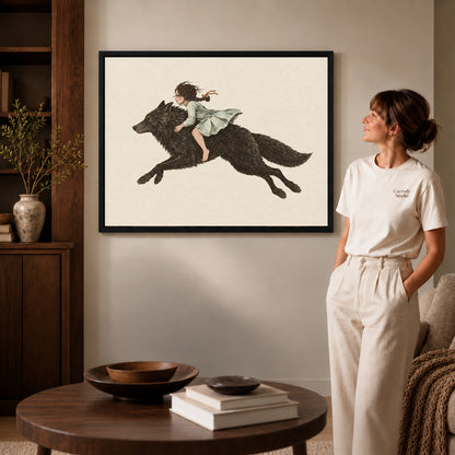 fairytale wolf rider canvas art in a black frame beside a woman and round wooden table.