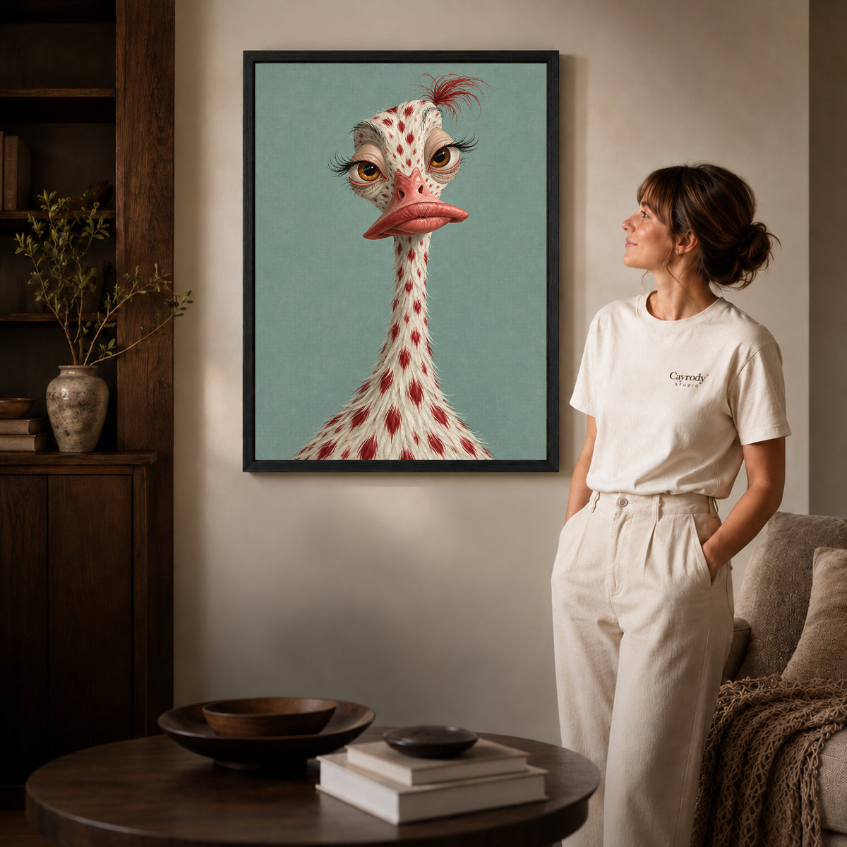 whimsical ostrich portrait canvas art in a black frame beside a woman and round wooden table.