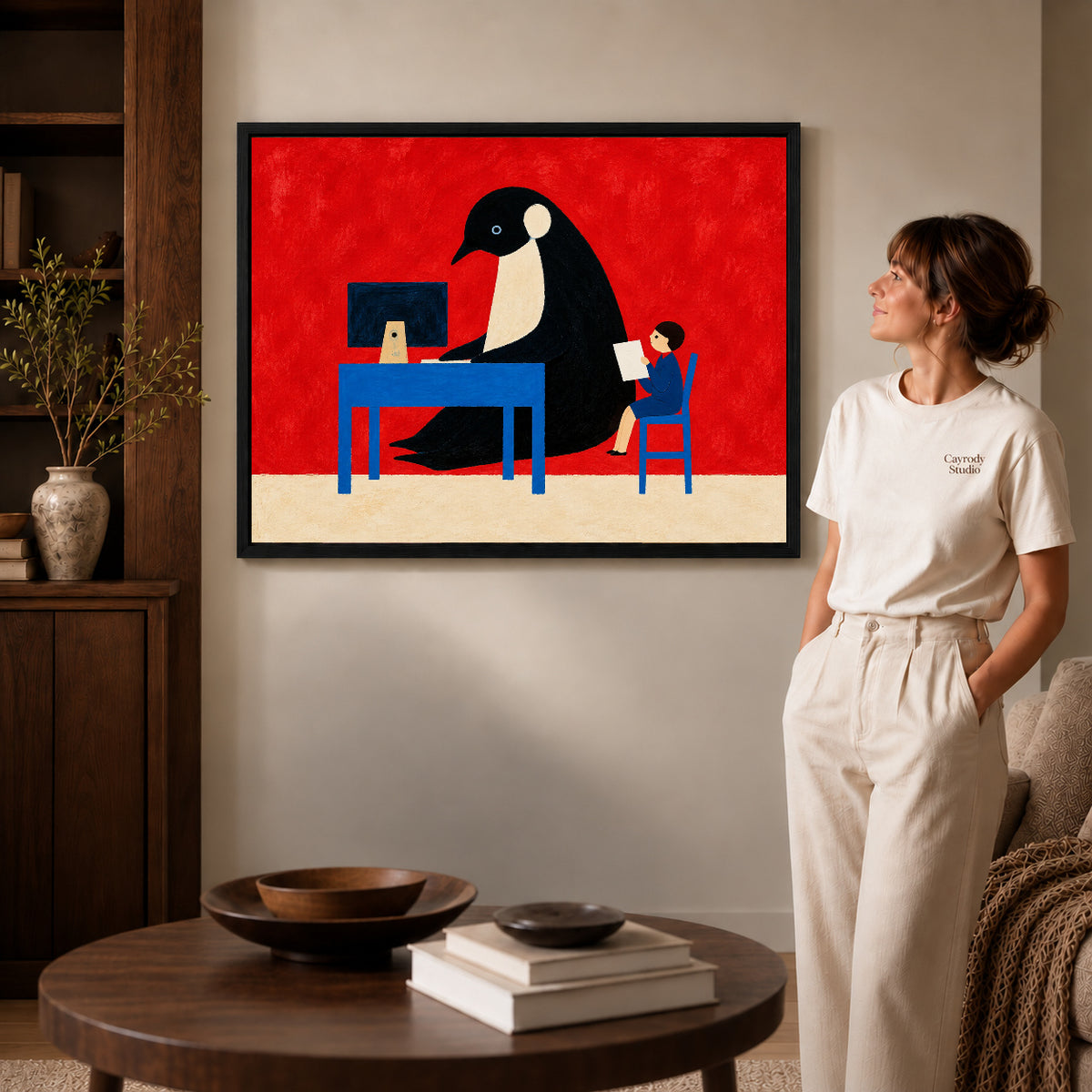 playful office penguin canvas art in a black frame beside a woman and round wooden table.