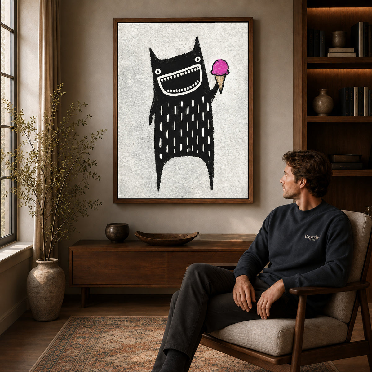 folk ice cream monster canvas art in a walnut frame above a console beside a seated man.