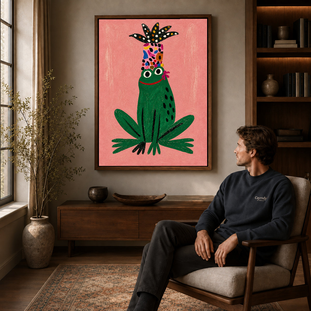 folk botanical frog canvas art in a walnut frame above a console beside a seated man.