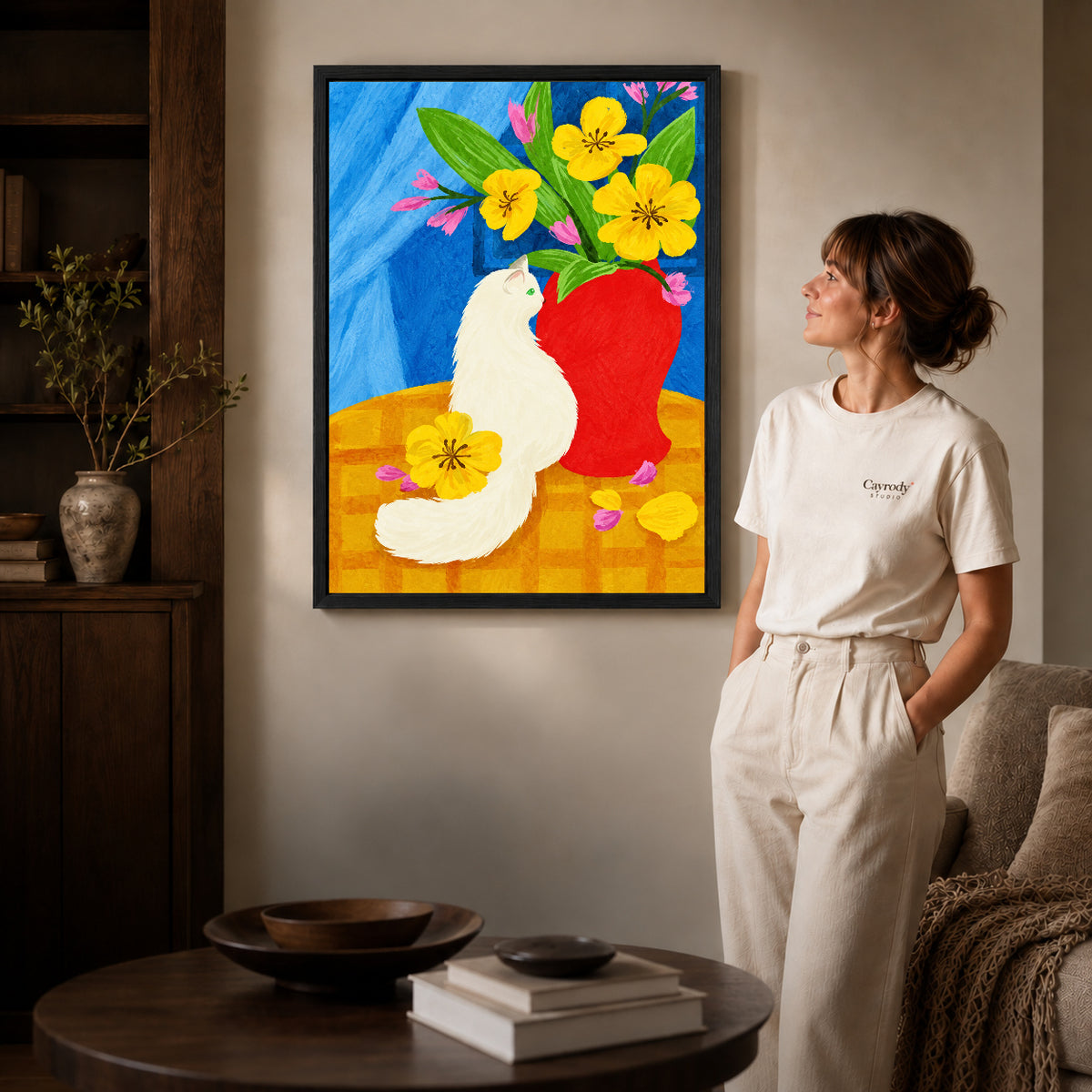 painterly white cat canvas art in a black frame beside a woman and round wooden table.
