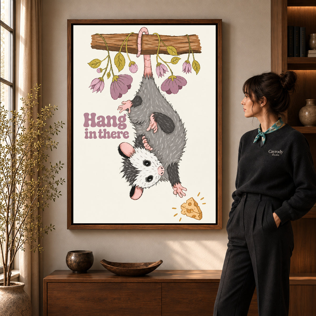 whimsical hanging opossum canvas art in a walnut frame beside a standing woman and wooden console.