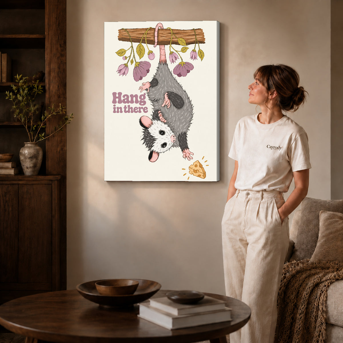 whimsical hanging opossum canvas art on gallery-wrapped canvas with natural edge shading beside a standing woman.