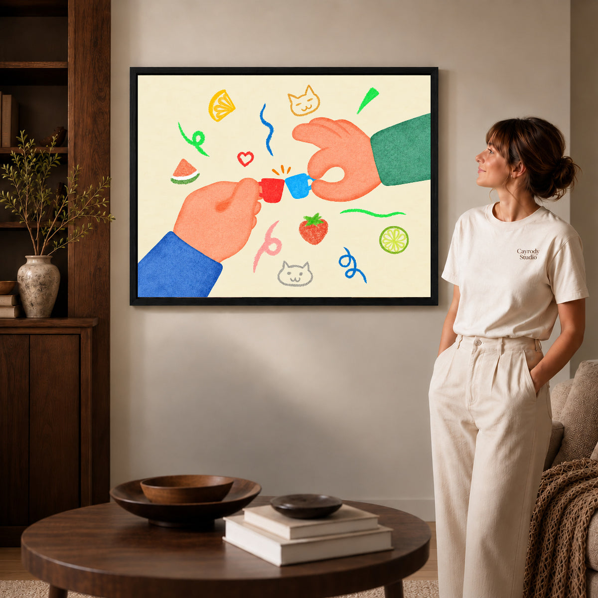 playful tiny cup cheers canvas art in a black frame beside a woman and round wooden table.