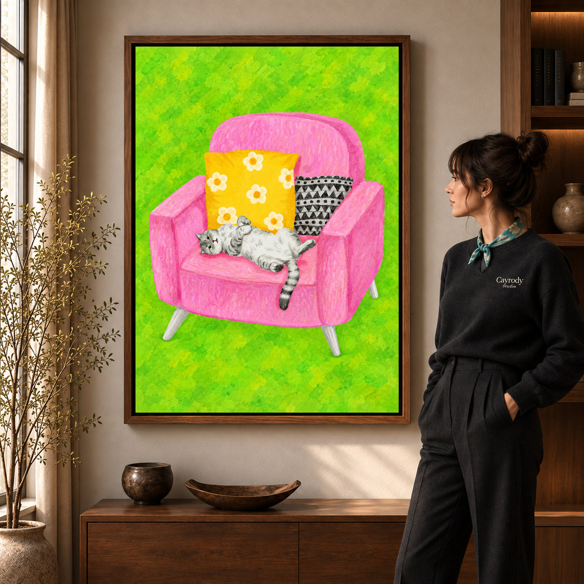 playful reclining cat canvas art in a walnut frame beside a standing woman and wooden console.