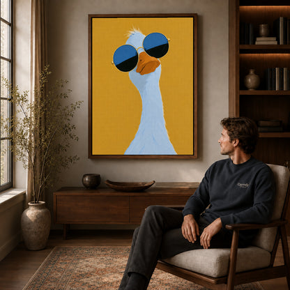 sunglasses goose portrait canvas art in a walnut frame above a console beside a seated man.