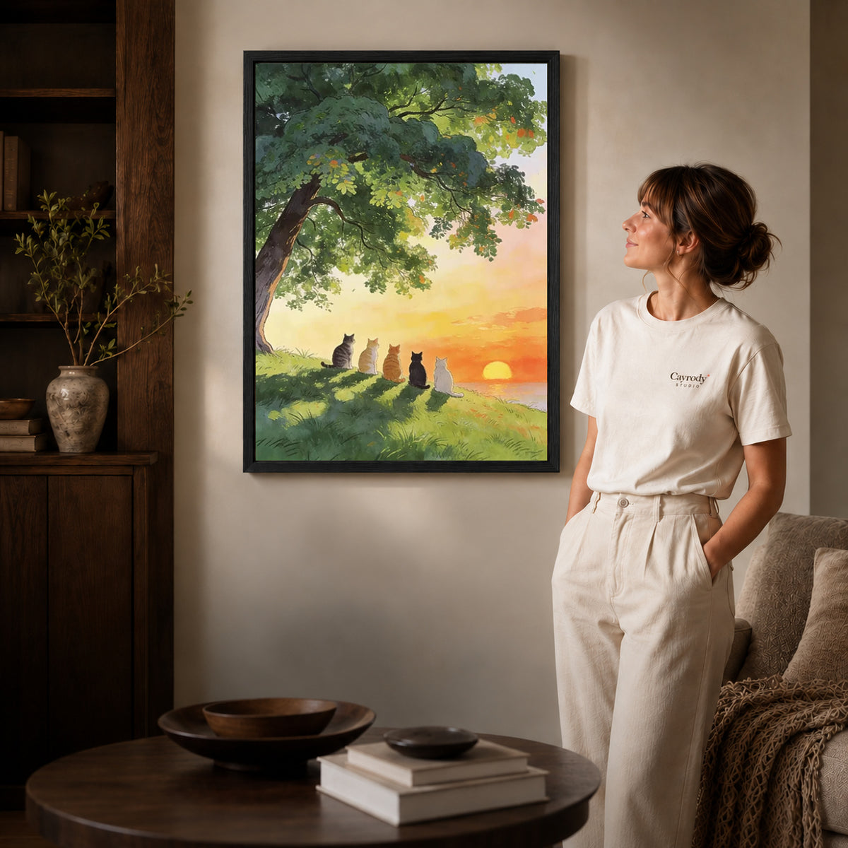 peaceful sunset cats canvas art in a black frame beside a woman and round wooden table.