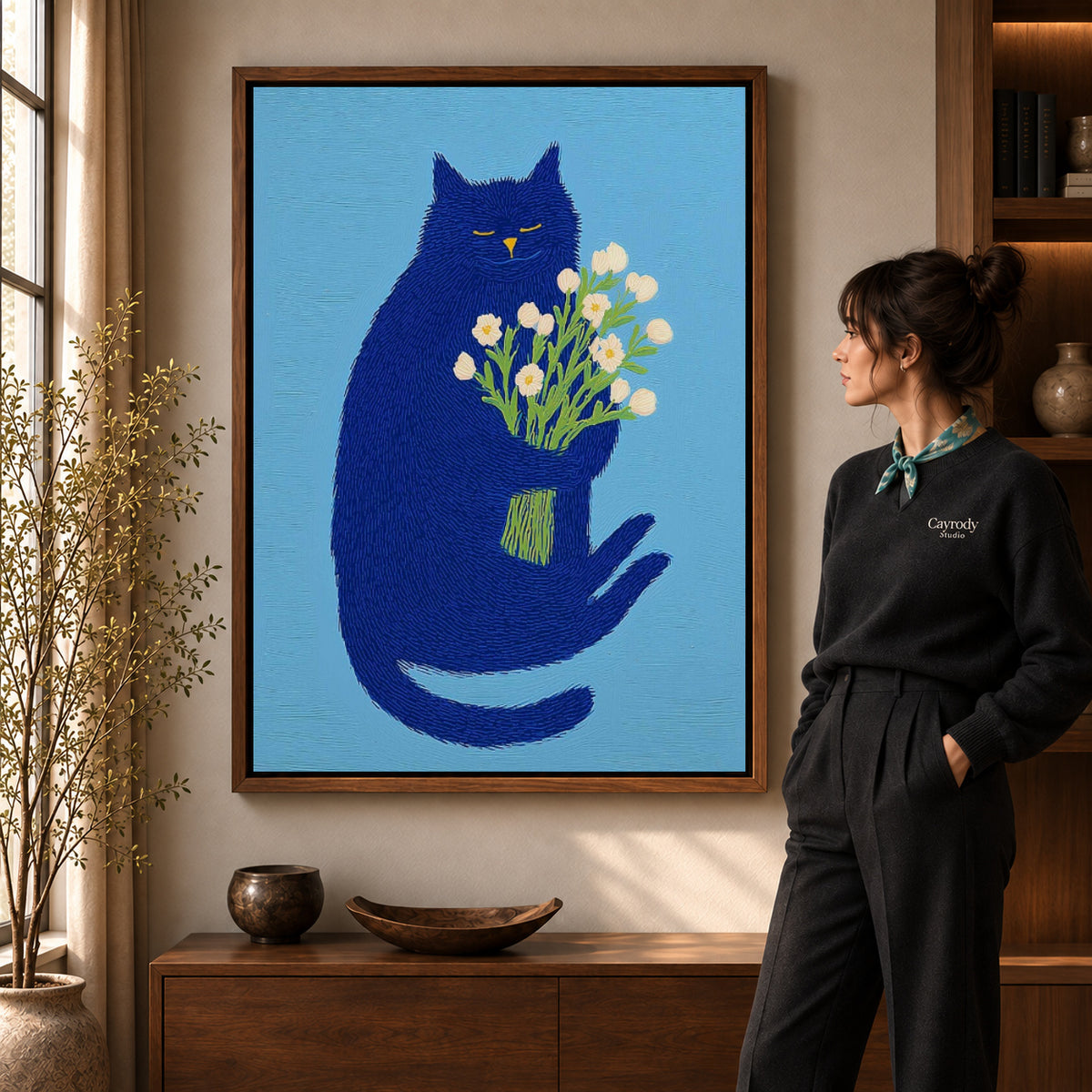 blue cat with flowers canvas art in a walnut frame beside a standing woman and wooden console.