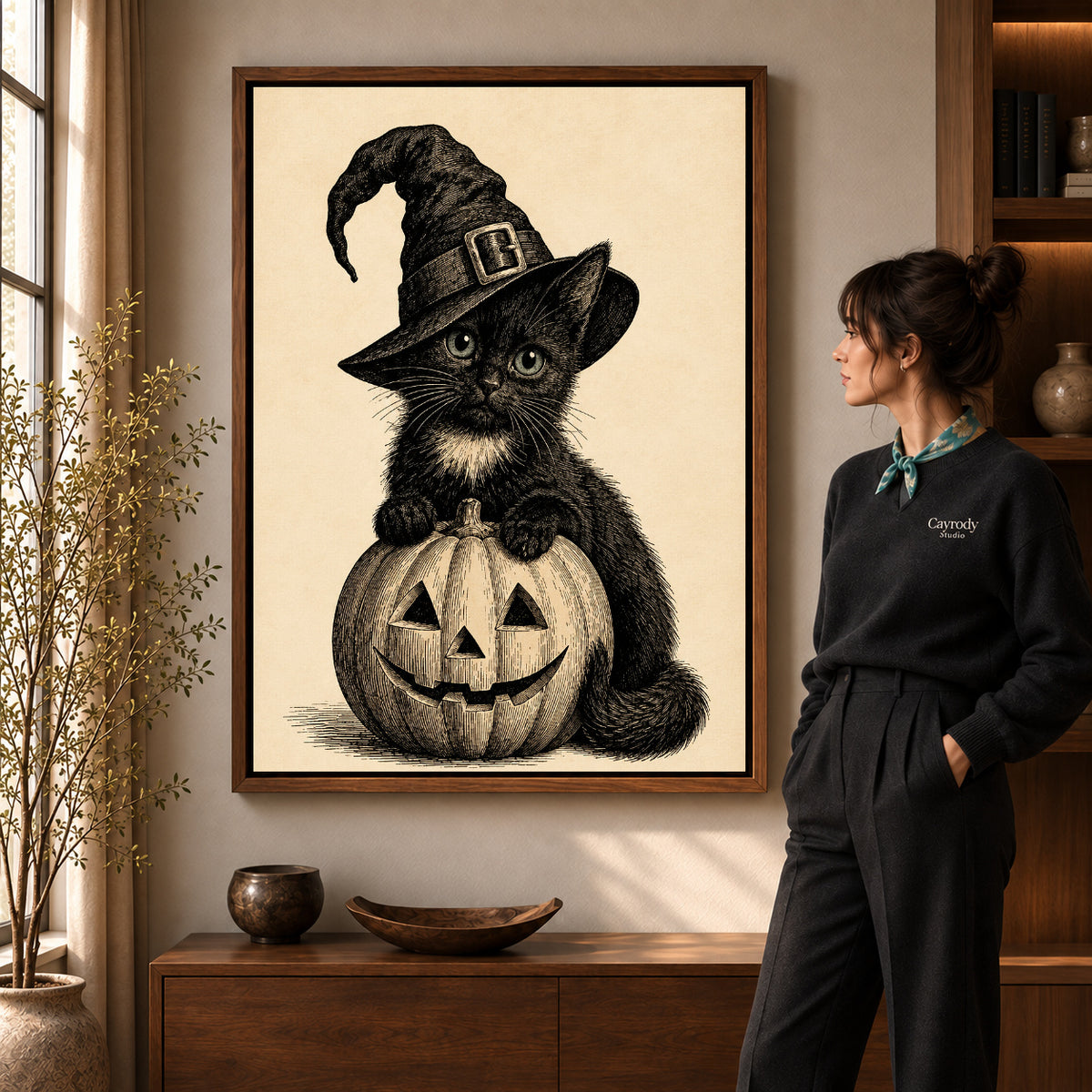 vintage pumpkin witch cat canvas art in a walnut frame beside a standing woman and wooden console.
