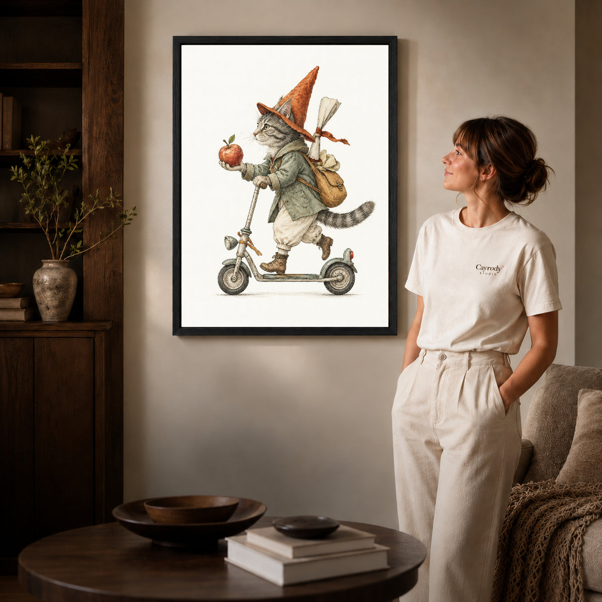 vintage scooter cat canvas art in a black frame beside a woman and round wooden table.