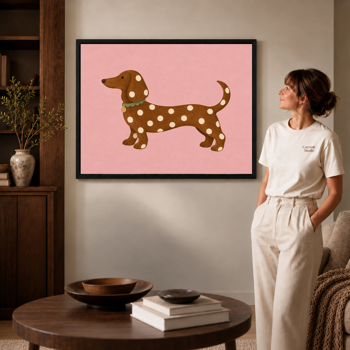 polka dot dachshund canvas art in a black frame beside a woman and round wooden table.
