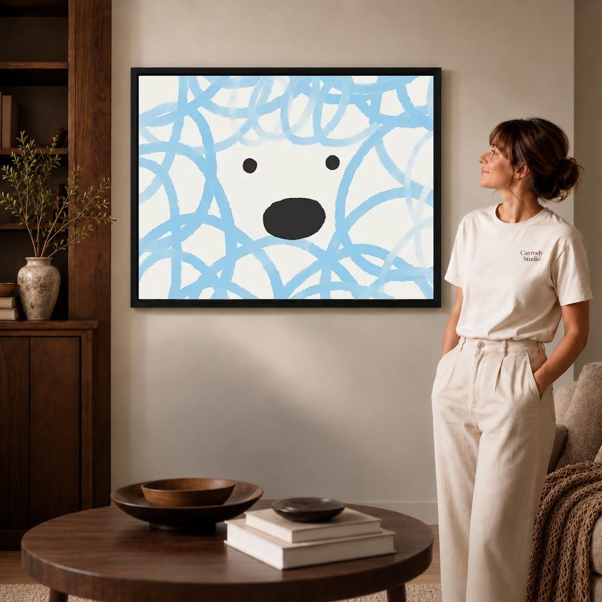 playful curly dog canvas art in a black frame beside a woman and round wooden table.