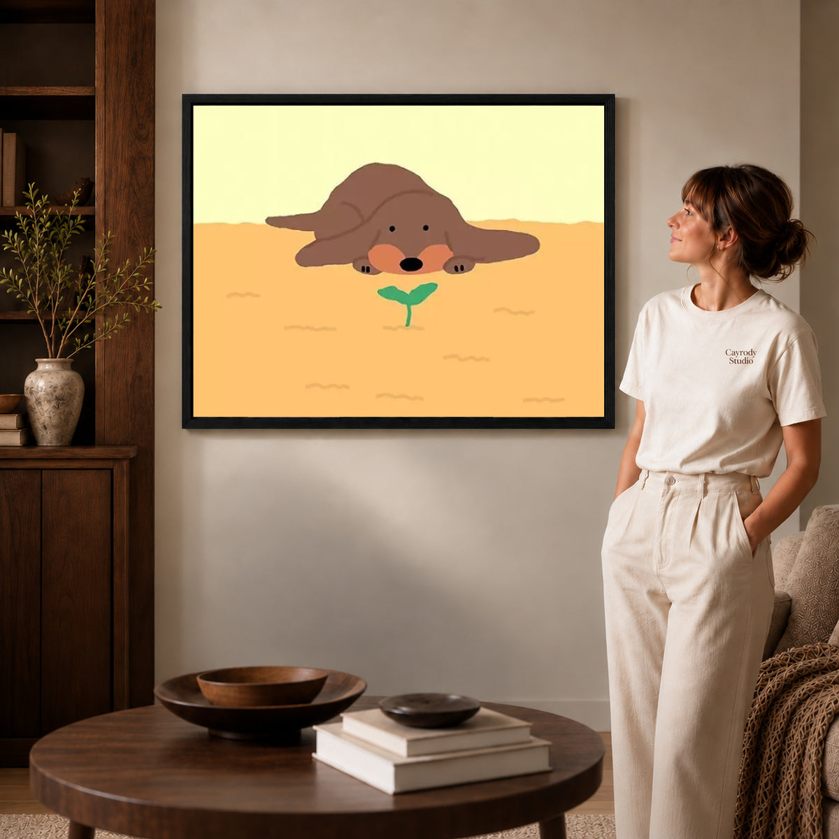 gentle puppy sprout canvas art in a black frame beside a woman and round wooden table.