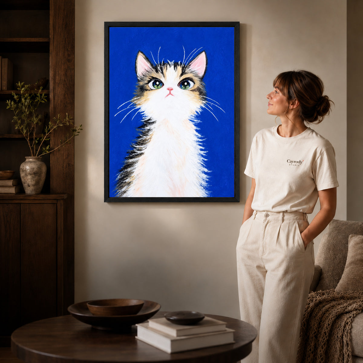 gentle blue kitten canvas art in a black frame beside a woman and round wooden table.