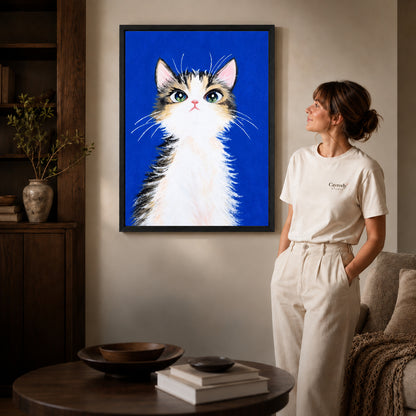 gentle blue kitten canvas art in a black frame beside a woman and round wooden table.