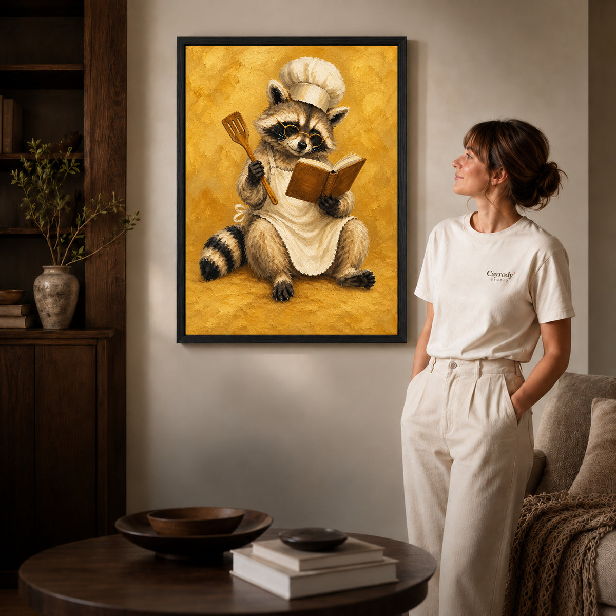 vintage raccoon chef canvas art in a black frame beside a woman and round wooden table.