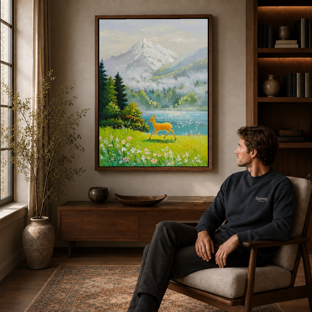 alpine deer meadow canvas art in a walnut frame above a console beside a seated man.