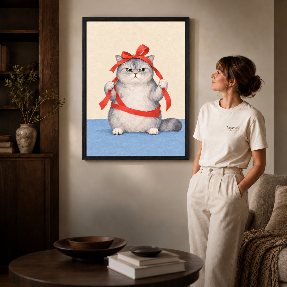grumpy ribbon cat canvas art in a black frame beside a woman and round wooden table.
