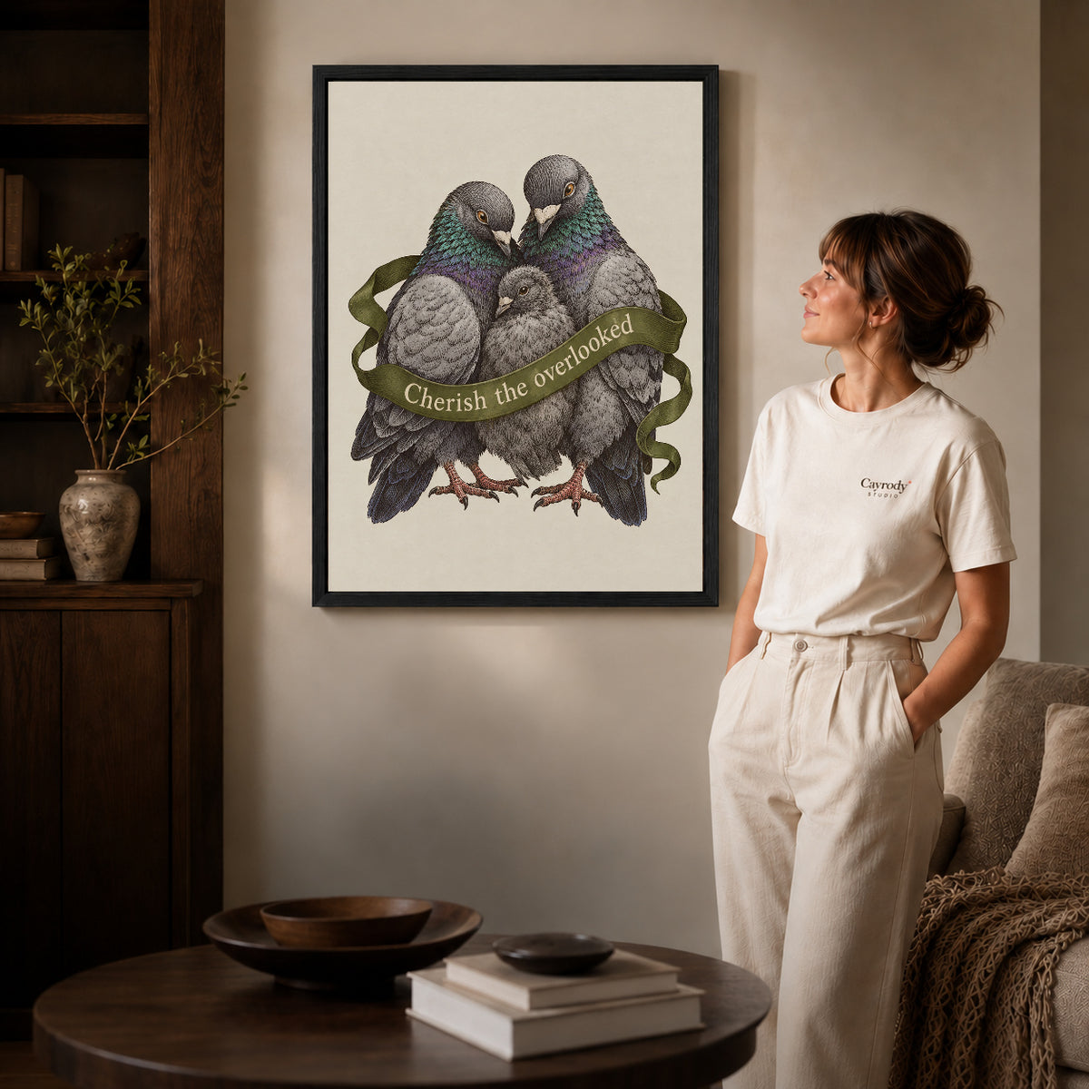 tender pigeon family canvas art in a black frame beside a woman and round wooden table.