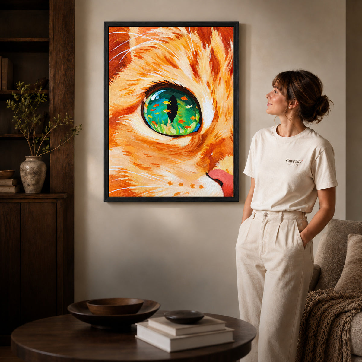 surreal aquarium cat canvas art in a black frame beside a woman and round wooden table.