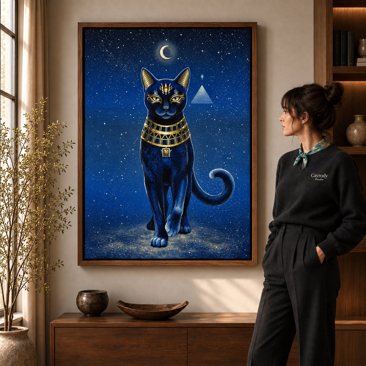 celestial golden cat canvas art in a walnut frame beside a standing woman and wooden console.