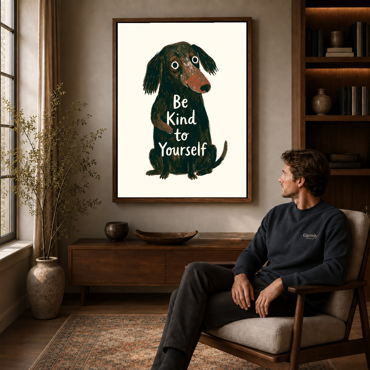 gentle kindness dog canvas art in a walnut frame above a console beside a seated man.
