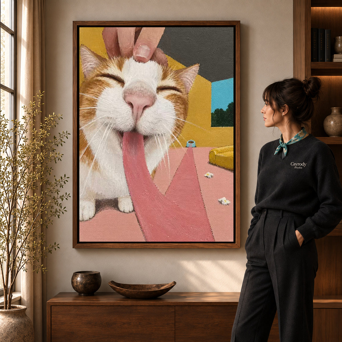 blissful long tongue cat canvas art in a walnut frame beside a standing woman and wooden console.