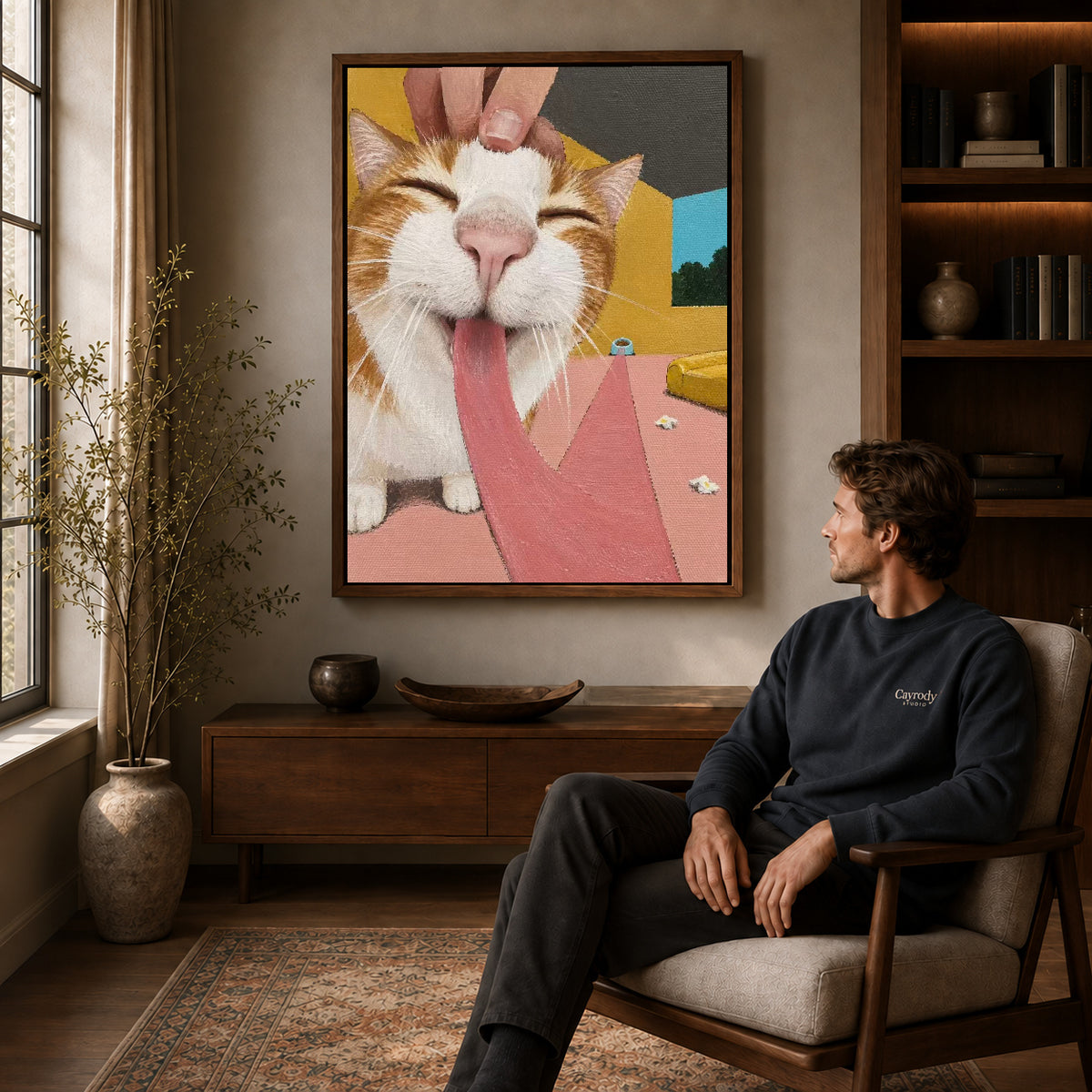 blissful long tongue cat canvas art in a walnut frame above a console beside a seated man.