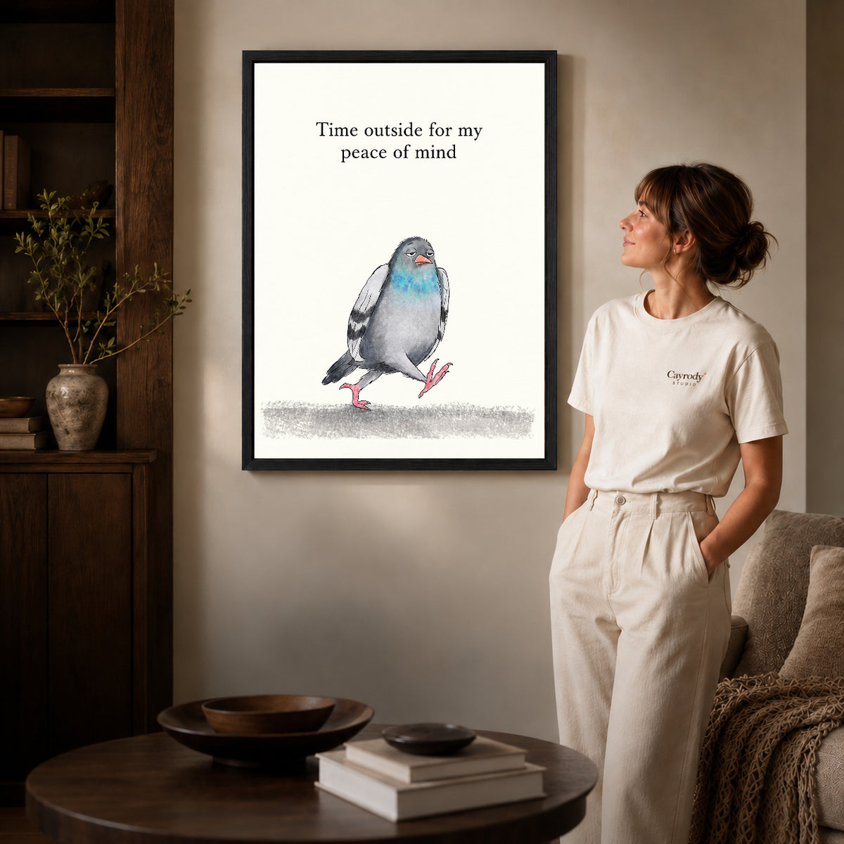 peaceful walking pigeon canvas art in a black frame beside a woman and round wooden table.