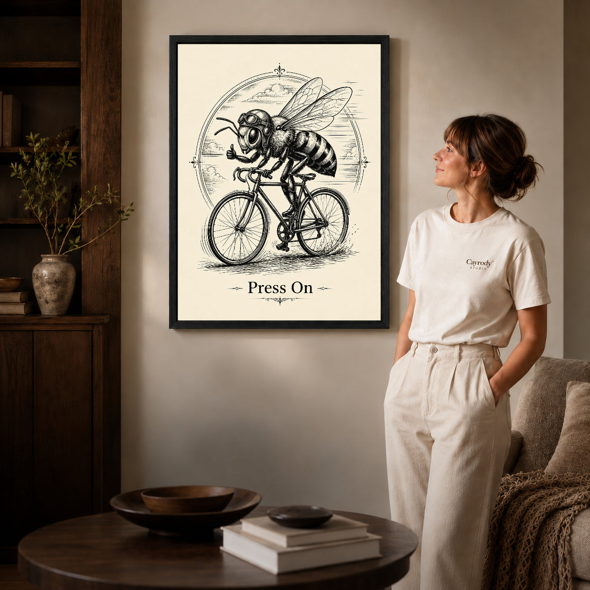 vintage cycling bee canvas art in a black frame beside a woman and round wooden table.