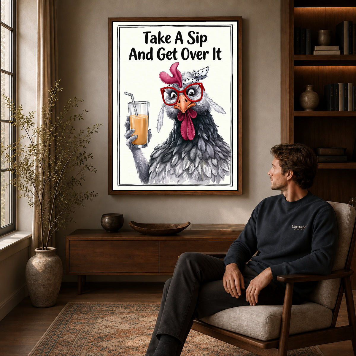 cheeky drink chicken canvas art in a walnut frame above a console beside a seated man.